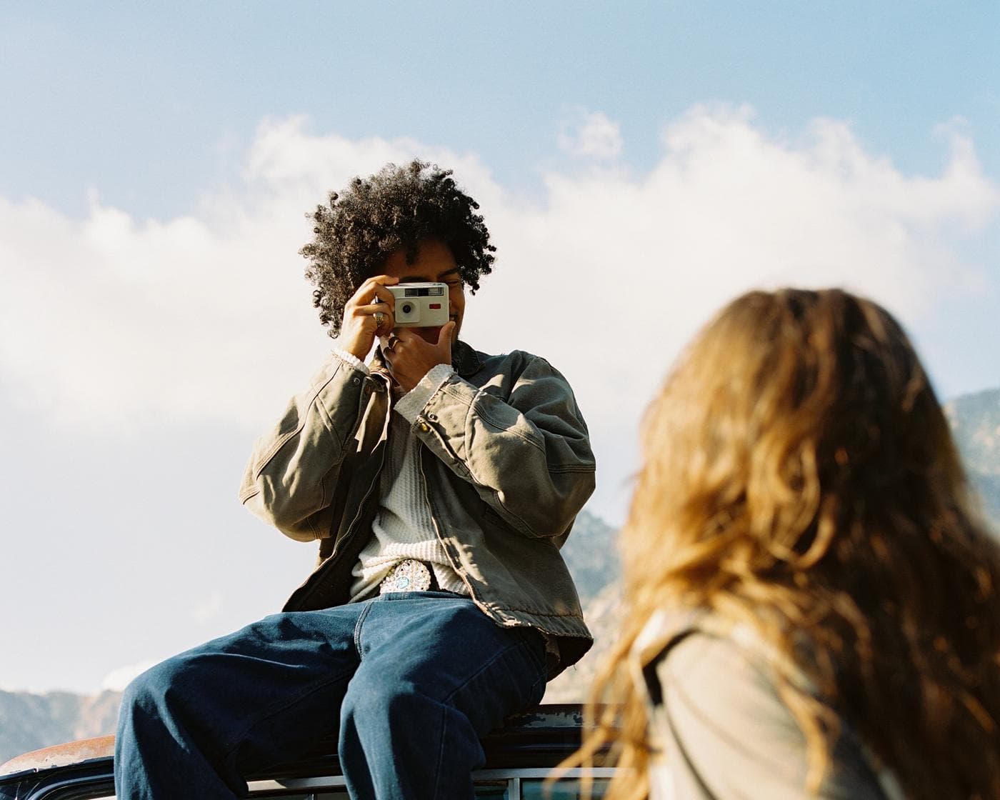 Man capturing woman on a truck in the sunshine wearing Long Weekend gear.