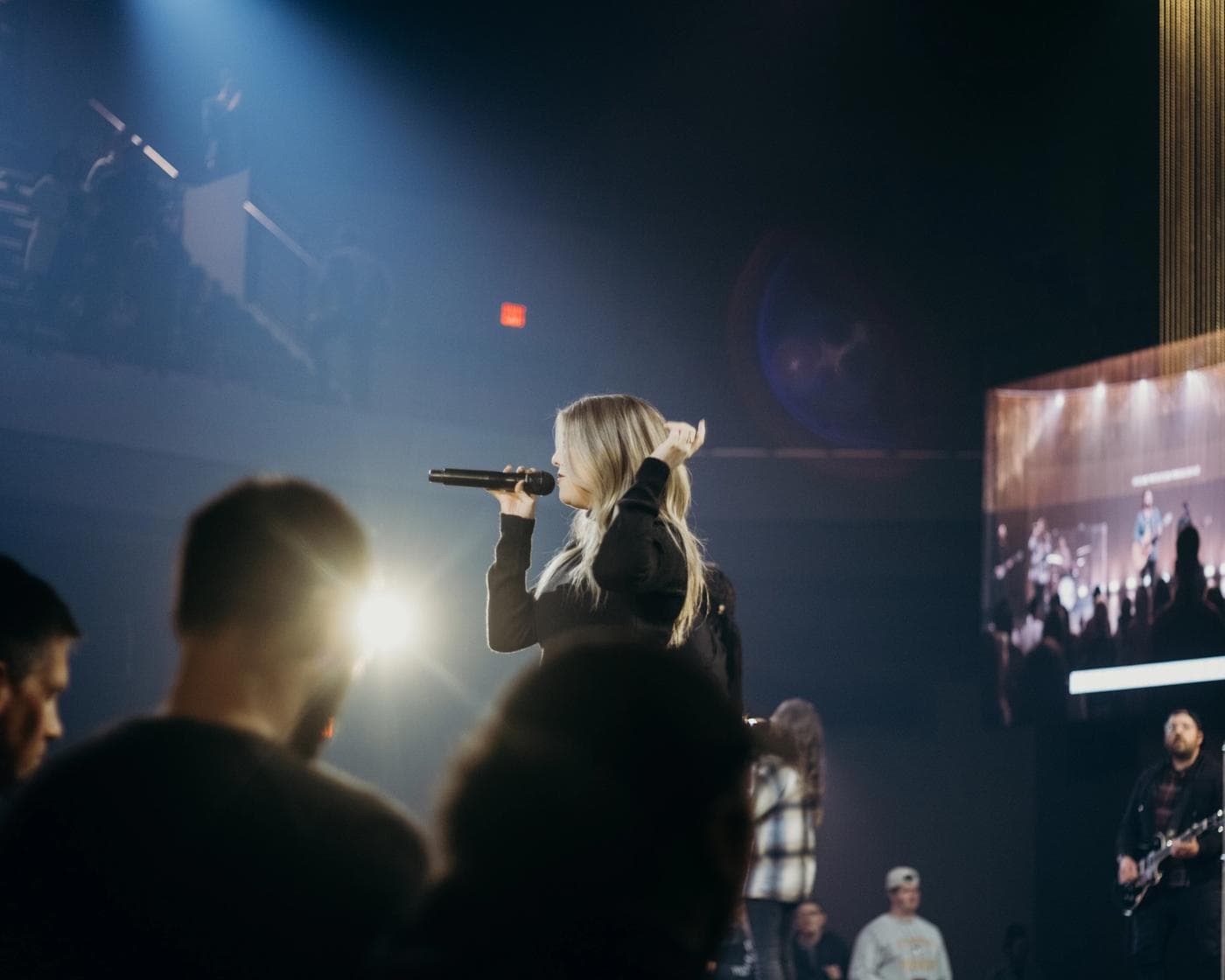 Woman singing songs inside a concert with lights and people.