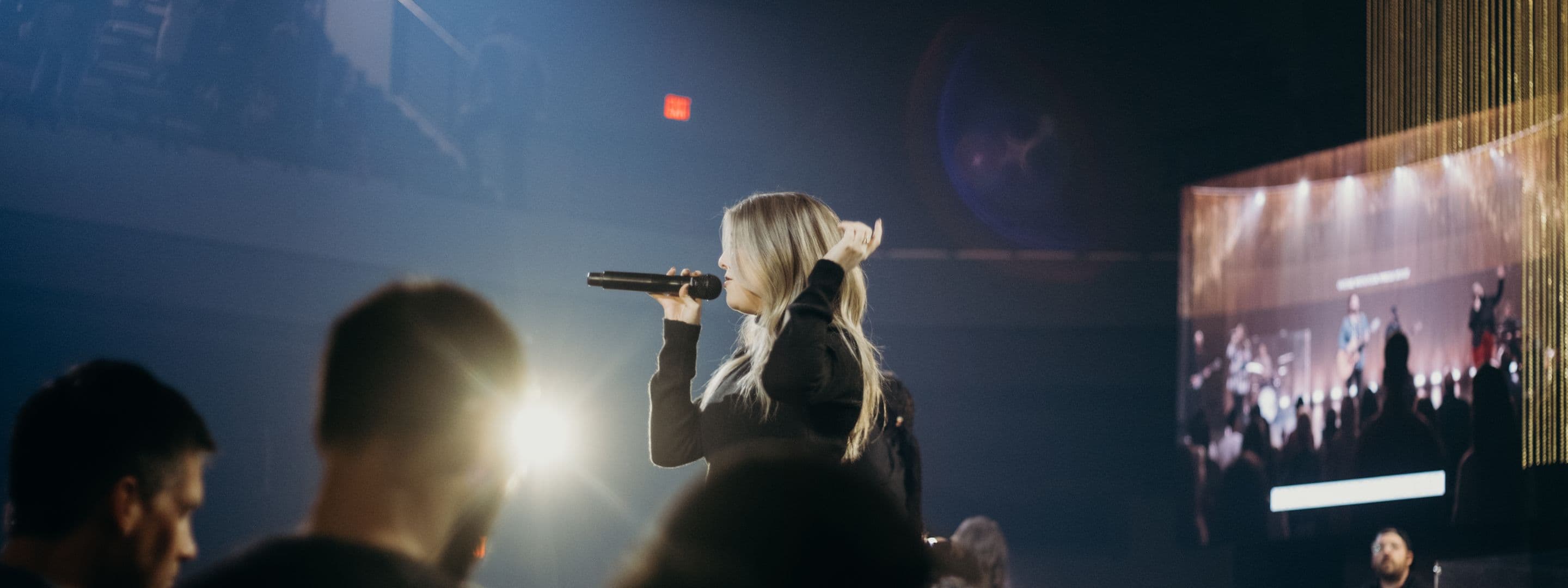 Woman singing songs inside a concert with lights and people.